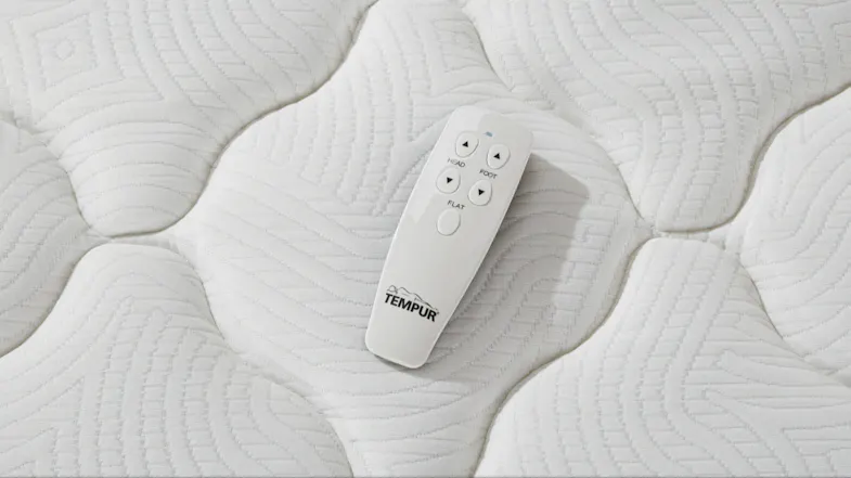 Top‑down close‑up of a white Tempur remote control resting on the mattress surface Top‑down close‑up of a white Tempur remote control resting on the mattress surface
