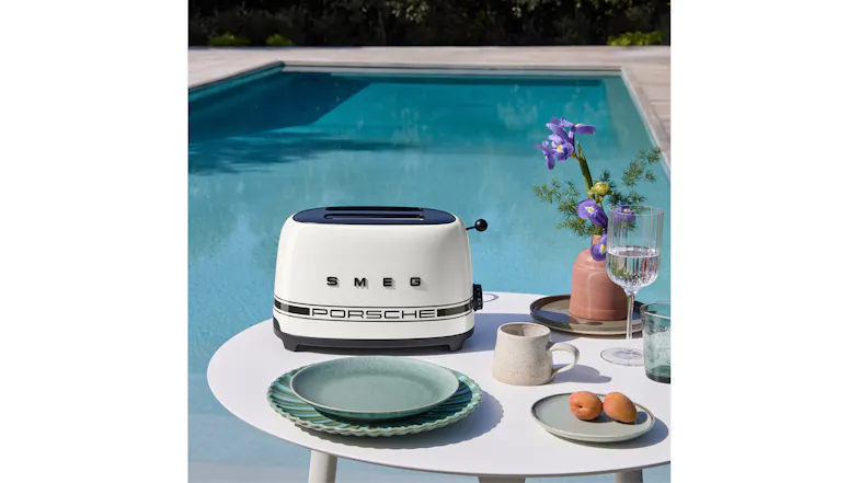 Smeg Porsche toaster on an outdoor table next to a pool, styled with breakfast items Smeg Porsche toaster on an outdoor table next to a pool, styled with breakfast items