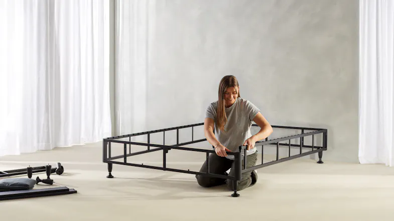 The bed frame is further assembled, showing a rectangular black metal structure The bed frame is further assembled, showing a rectangular black metal structure