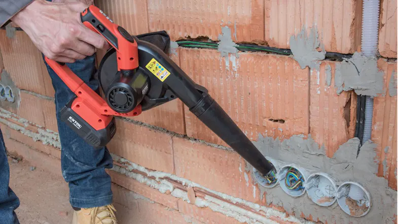 A worker using a cordless leaf blower to clean electrical conduit openings in a brick wall A worker using a cordless leaf blower to clean electrical conduit openings in a brick wall