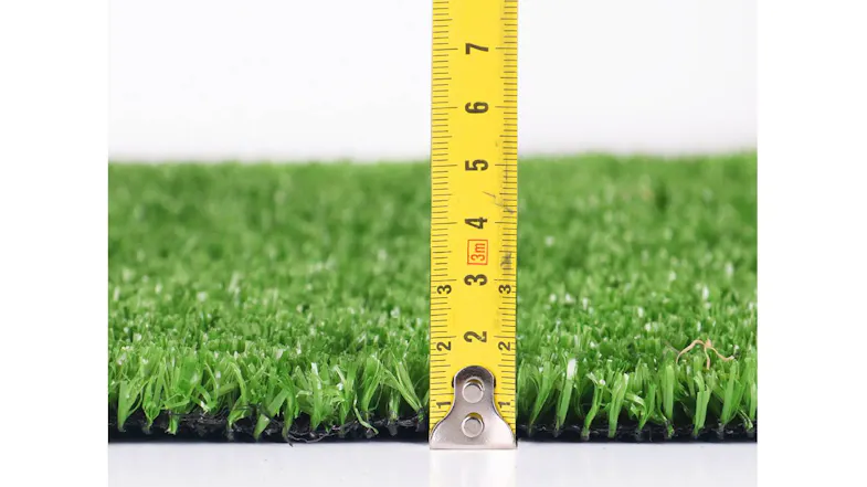 Side view of olive green artificial grass with a yellow measuring tape placed vertically against the edge Side view of olive green artificial grass with a yellow measuring tape placed vertically against the edge