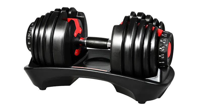 Adjustable dumbbell set with black plates and red accents resting on a moulded storage cradle Adjustable dumbbell set with black plates and red accents resting on a moulded storage cradle