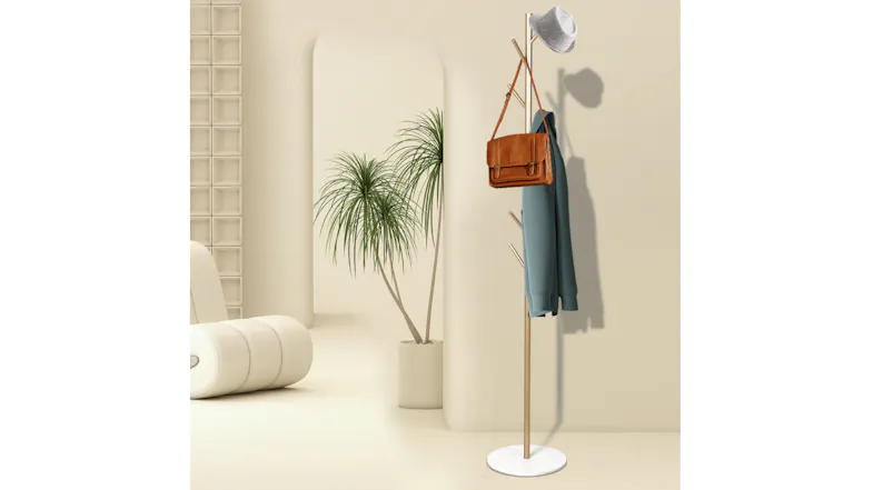 Gold coat rack styled in a minimalist room, holding a hat, bag, and coat near a plant and seating Gold coat rack styled in a minimalist room, holding a hat, bag, and coat near a plant and seating
