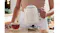 A person is lifting the cream kettle off its chrome base A person is lifting the cream kettle off its chrome base