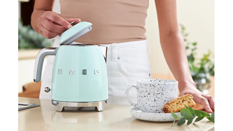 A person opening the pastel green lid of the SMEG kettle in a modern kitchen A person opening the pastel green lid of the SMEG kettle in a modern kitchen
