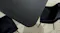 Close-up of the dark wood-look tabletop with rounded corner edges, and surrounding black dining chairs Close-up of the dark wood-look tabletop with rounded corner edges, and surrounding black dining chairs