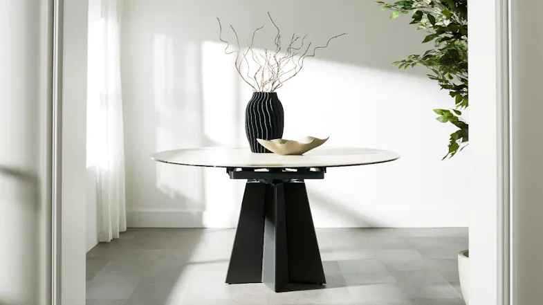 Oval dining table shown alone, featuring a light-toned top and bold black geometric pedestal base Oval dining table shown alone, featuring a light-toned top and bold black geometric pedestal base