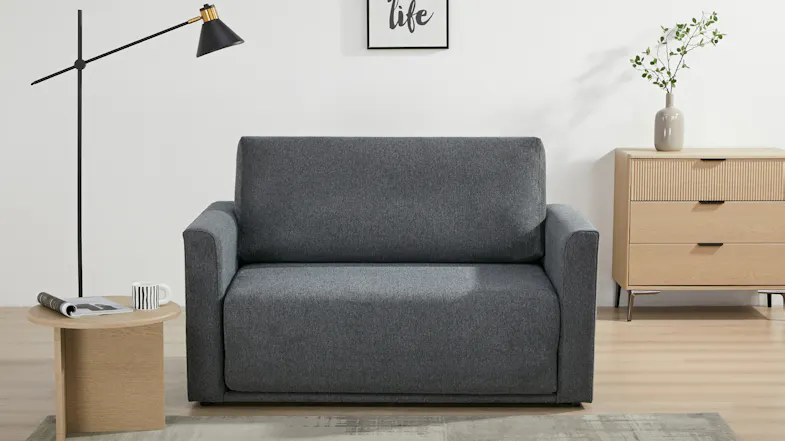 Front view of the Oliver fabric sofa bed in dark grey upholstery, shown as a compact two‑seat sofa Front view of the Oliver fabric sofa bed in dark grey upholstery, shown as a compact two‑seat sofa