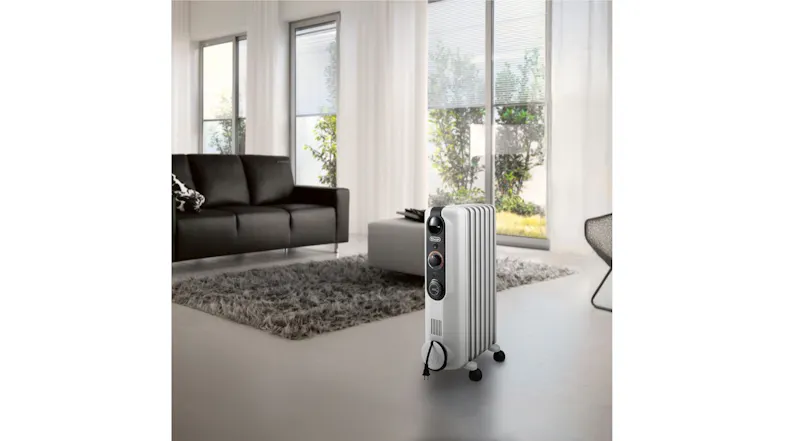 Portable electric radiator heater on wheels in a sunlit living space with rug, sofa, and glass doors Portable electric radiator heater on wheels in a sunlit living space with rug, sofa, and glass doors