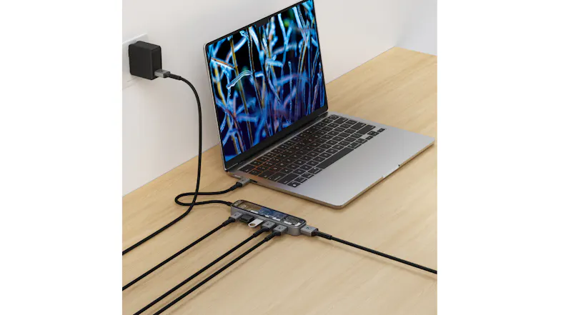 Laptop plugged into power and USB-C hub with multiple accessories connected on a wooden desk Laptop plugged into power and USB-C hub with multiple accessories connected on a wooden desk