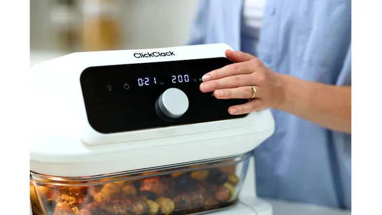 Close-up of the ClickClack air fryer control panel with dial and digital display, hand adjusting settings, food visible below Close-up of the ClickClack air fryer control panel with dial and digital display, hand adjusting settings, food visible below