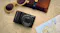 Black Panasonic Lumix camera on a textured surface beside sunglasses, a leather case, and a travel map Black Panasonic Lumix camera on a textured surface beside sunglasses, a leather case, and a travel map