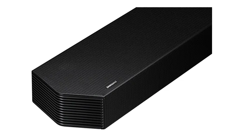 A close-up angled view of a black soundbar end with layered grille detailing and the Samsung logo A close-up angled view of a black soundbar end with layered grille detailing and the Samsung logo