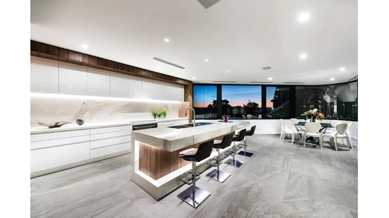Modern open-plan kitchen with a marble island, bar stools, white cabinets, and large windows overlooking a sunset Modern open-plan kitchen with a marble island, bar stools, white cabinets, and large windows overlooking a sunset