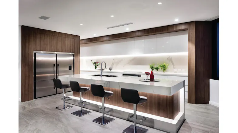 Sleek kitchen with a marble island, four black bar stools, a stainless steel fridge, and wood-accent cabinetry Sleek kitchen with a marble island, four black bar stools, a stainless steel fridge, and wood-accent cabinetry