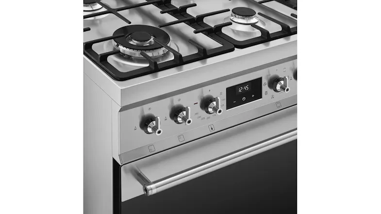 A close-up view of the Smeg freestanding oven control panel and gas cooktop burners in stainless steel finish with knobs A close-up view of the Smeg freestanding oven control panel and gas cooktop burners in stainless steel finish with knobs