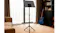 Full view of a black metal music stand set on a tripod base in the living room, beside a bookshelf and a blue acoustic guitar indoors Full view of a black metal music stand set on a tripod base in the living room, beside a bookshelf and a blue acoustic guitar indoors