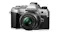 Silver OM System OM‑5 camera with attached 25mm lens, showing textured grip and control dials Silver OM System OM‑5 camera with attached 25mm lens, showing textured grip and control dials