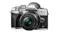 A silver Olympus OM‑D camera with a 25mm lens, textured grip, and control dials A silver Olympus OM‑D camera with a 25mm lens, textured grip, and control dials