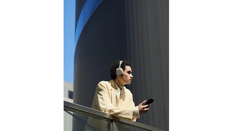 A man leaning on a handrail while using his device and headphones A man leaning on a handrail while using his device and headphones