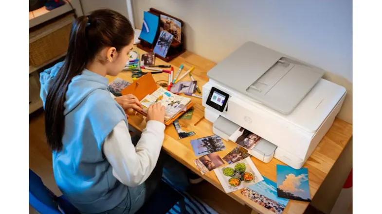 Printer in use on a desk surrounded by printed photos and craft materials. A person arranges printed images Printer in use on a desk surrounded by printed photos and craft materials. A person arranges printed images