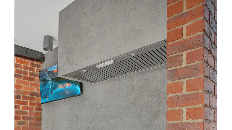 Modern stainless steel range hood with built-in LED lights mounted under a concrete wall between red brick columns Modern stainless steel range hood with built-in LED lights mounted under a concrete wall between red brick columns