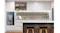 A kitchen featuring a Schweigen integrated rangehood, white cabinets, countertop, bar stools, and a built-in oven A kitchen featuring a Schweigen integrated rangehood, white cabinets, countertop, bar stools, and a built-in oven