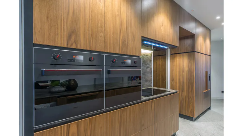 Contemporary kitchen with wood cabinetry, built-in double ovens, cooktop niche, and sleek integrated rangehood Contemporary kitchen with wood cabinetry, built-in double ovens, cooktop niche, and sleek integrated rangehood