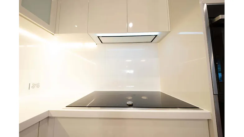 Modern white kitchen with ceramic cooktop, glossy cabinetry, and concealed white glass undermount rangehood above cooktop Modern white kitchen with ceramic cooktop, glossy cabinetry, and concealed white glass undermount rangehood above cooktop