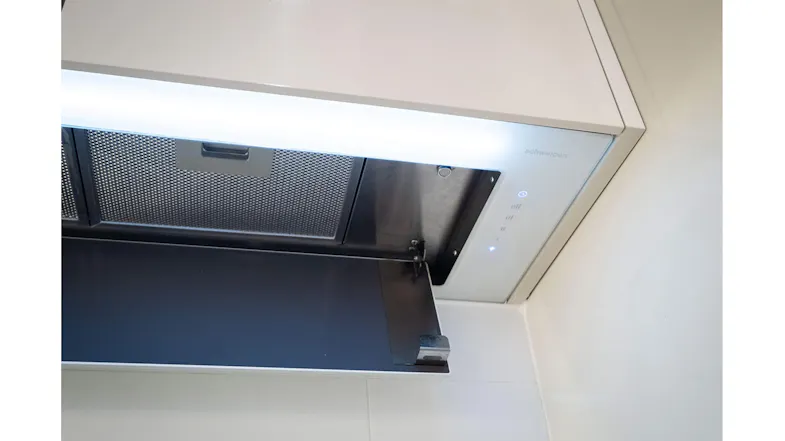 Installed white glass undermount rangehood with open panel, LED lighting, and visible mesh filter in modern tiled kitchen Installed white glass undermount rangehood with open panel, LED lighting, and visible mesh filter in modern tiled kitchen