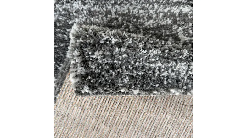 Close-up of the rug’s corner folded back, showing thick, plush pile in mixed charcoal, grey, and white tones Close-up of the rug’s corner folded back, showing thick, plush pile in mixed charcoal, grey, and white tones