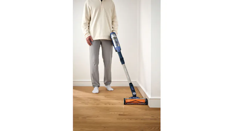 Person vacuuming along a wall edge on hardwood flooring with a Shark cordless stick vacuum Person vacuuming along a wall edge on hardwood flooring with a Shark cordless stick vacuum