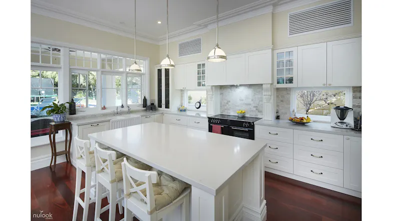Bright white kitchen with a central island, bar stools, pendant lights, and large windows for natural light Bright white kitchen with a central island, bar stools, pendant lights, and large windows for natural light