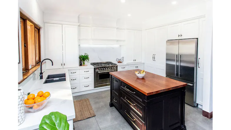 Spacious white kitchen with stainless fridge, gas range, marble counters, black island with wooden top, sink, fruit bowl, and rangehood Spacious white kitchen with stainless fridge, gas range, marble counters, black island with wooden top, sink, fruit bowl, and rangehood