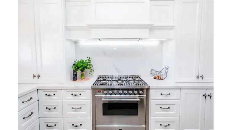 Bright white kitchen with shaker cabinets, marble backsplash, and stainless-steel gas range, framed by drawers, plants, and egg basket Bright white kitchen with shaker cabinets, marble backsplash, and stainless-steel gas range, framed by drawers, plants, and egg basket