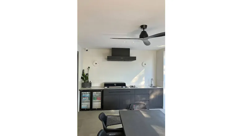 Minimalist outdoor kitchen with black rangehood, built-in grill, sink, and glass-front fridge Minimalist outdoor kitchen with black rangehood, built-in grill, sink, and glass-front fridge