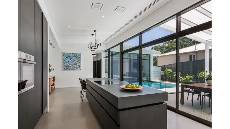 Sleek kitchen with a black island counter, a wooden table and an outdoor pool visible through glass panels Sleek kitchen with a black island counter, a wooden table and an outdoor pool visible through glass panels