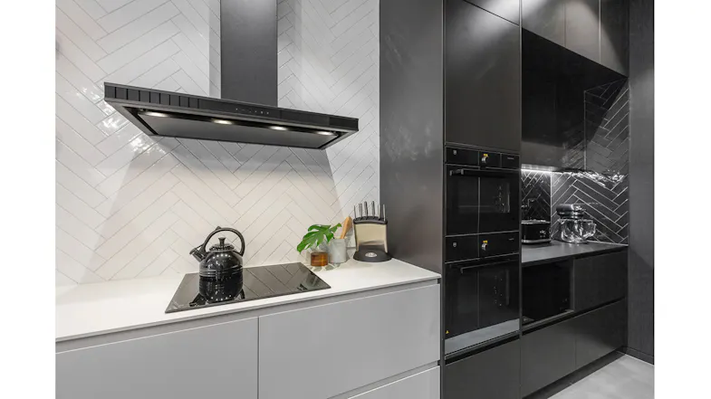Elegant modern kitchen detail with cooktop, black rangehood lights, and textured white tile backsplash Elegant modern kitchen detail with cooktop, black rangehood lights, and textured white tile backsplash