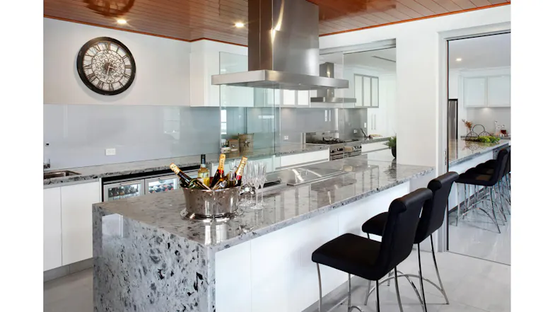 Kitchen interior with island range hood, glass backsplash, and sleek white cabinets Kitchen interior with island range hood, glass backsplash, and sleek white cabinets