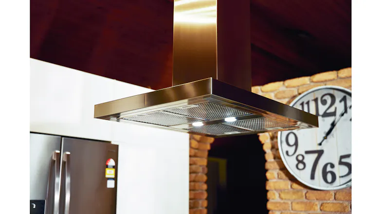 Island rangehood detail with built-in lights and metal filters against a brick wall backdrop Island rangehood detail with built-in lights and metal filters against a brick wall backdrop