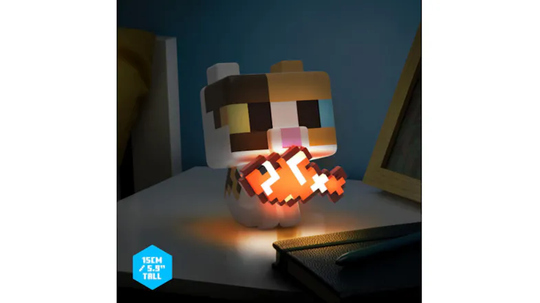 A blocky, cat-shaped Paladone GloBuddies novelty light figure holding a glowing orange, pixel-style fish on a desk in a dimly lit room A blocky, cat-shaped Paladone GloBuddies novelty light figure holding a glowing orange, pixel-style fish on a desk in a dimly lit room