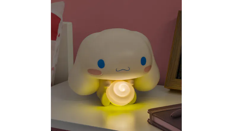 A small white bunny Paladone GloBuddies night light, glowing yellow, is placed on a bedside table beside a notebook and a photo frame A small white bunny Paladone GloBuddies night light, glowing yellow, is placed on a bedside table beside a notebook and a photo frame