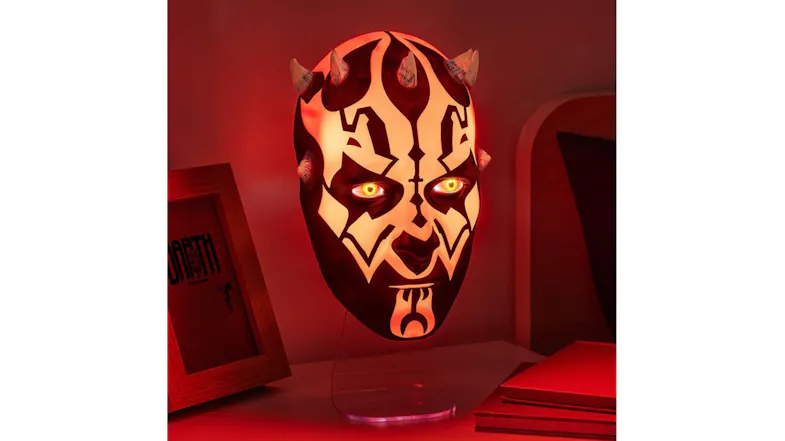 Same horned Paladone mask lamp glowing red with lit eyes, casting warm light on nearby books and framed artwork Same horned Paladone mask lamp glowing red with lit eyes, casting warm light on nearby books and framed artwork