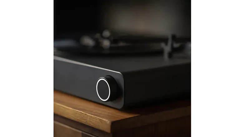 Close-up of the Victrola Stream black turntable front corner showing textured finish and circular control knob on wood cabinet Close-up of the Victrola Stream black turntable front corner showing textured finish and circular control knob on wood cabinet