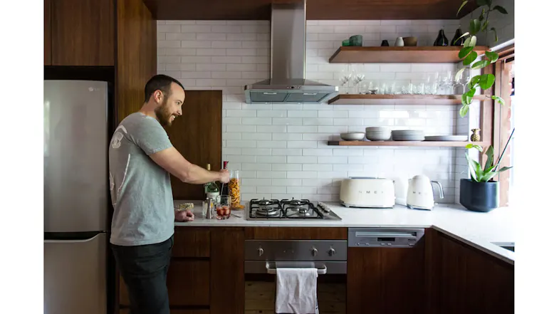 A man is standing at a kitchen counter preparing a drink beside a stovetop under a stainless steel rangehood A man is standing at a kitchen counter preparing a drink beside a stovetop under a stainless steel rangehood