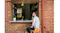 Person seated at an outdoor window bar, holding a drink, looking into a modern kitchen framed by a brick wall Person seated at an outdoor window bar, holding a drink, looking into a modern kitchen framed by a brick wall