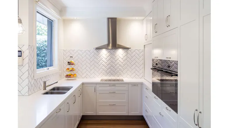 Bright white kitchen with stainless steel rangehood, herringbone tile splashback, double sink and sleek cabinetry Bright white kitchen with stainless steel rangehood, herringbone tile splashback, double sink and sleek cabinetry
