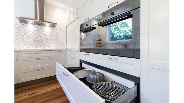Modern kitchen with stainless steel rangehood, built-in ovens, open drawer storage and white cabinetry layout Modern kitchen with stainless steel rangehood, built-in ovens, open drawer storage and white cabinetry layout