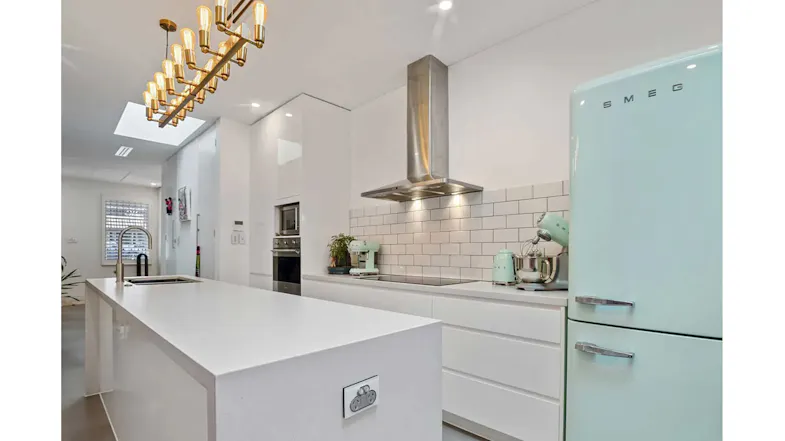Bright modern kitchen with stainless steel wall-mounted rangehood, white cabinetry, subway tile splashback and pastel fridge Bright modern kitchen with stainless steel wall-mounted rangehood, white cabinetry, subway tile splashback and pastel fridge