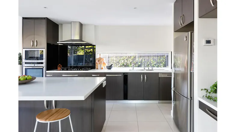 Modern kitchen with a stainless steel rangehood, dark cabinetry, island bench, window splashback and integrated appliances Modern kitchen with a stainless steel rangehood, dark cabinetry, island bench, window splashback and integrated appliances